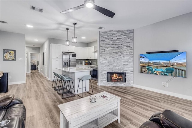 living room with visible vents, baseboards, a stone fireplace, light wood-style flooring, and a ceiling fan