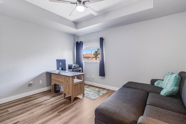 office featuring a tray ceiling, wood finished floors, baseboards, and ceiling fan