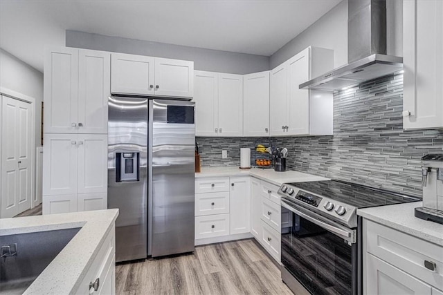 kitchen featuring white cabinets, appliances with stainless steel finishes, wall chimney range hood, light wood-type flooring, and backsplash