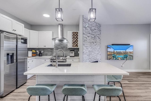 kitchen with light wood finished floors, a sink, wall chimney exhaust hood, stainless steel fridge, and backsplash