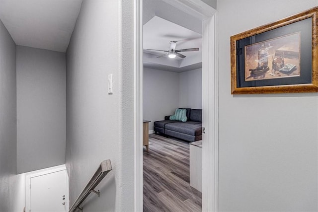 corridor with baseboards, a raised ceiling, and wood finished floors