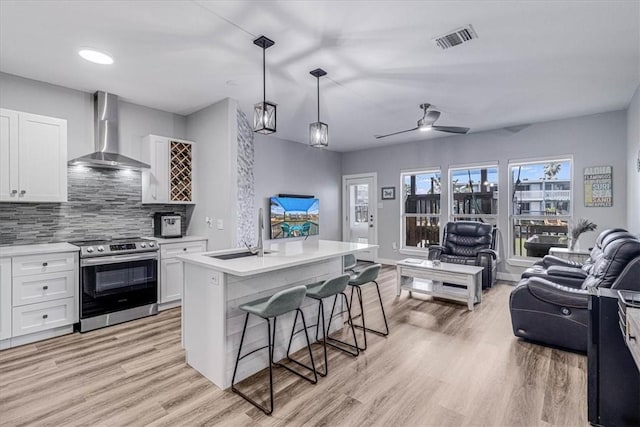 kitchen featuring a sink, stainless steel range with electric cooktop, white cabinets, wall chimney range hood, and open floor plan