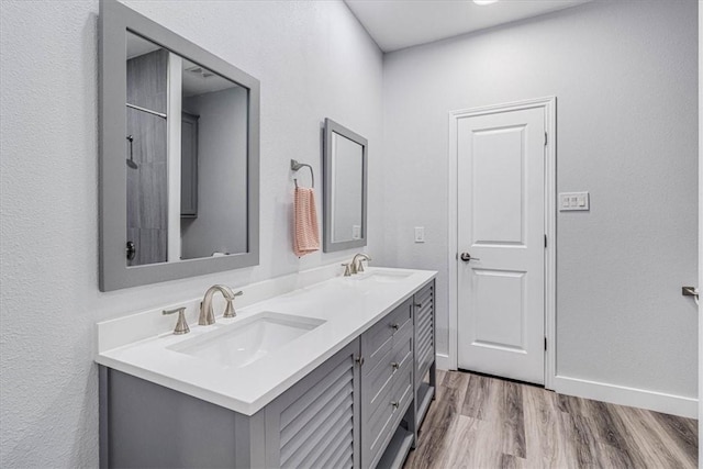 full bath featuring double vanity, wood finished floors, baseboards, and a sink