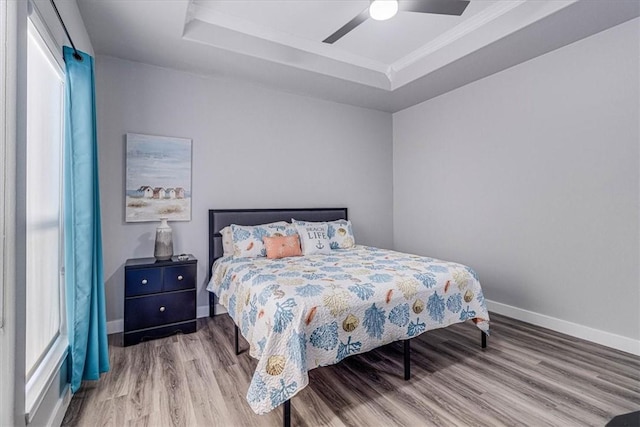 bedroom featuring a raised ceiling, wood finished floors, baseboards, and ceiling fan