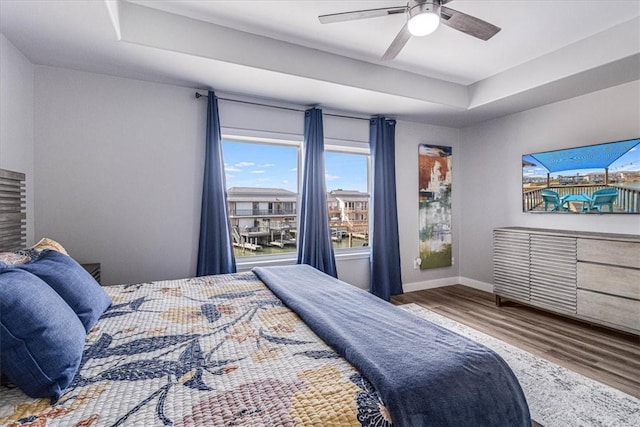 bedroom with ceiling fan, a tray ceiling, baseboards, and wood finished floors