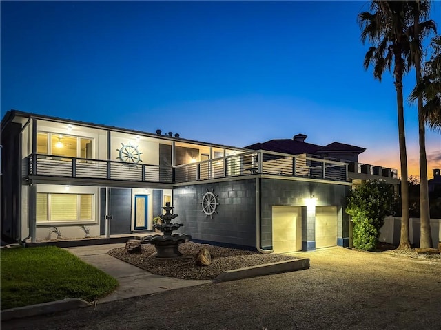 back house at dusk featuring a balcony and a garage