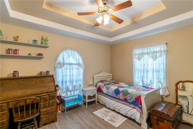 bedroom featuring ceiling fan, light hardwood / wood-style floors, and a raised ceiling