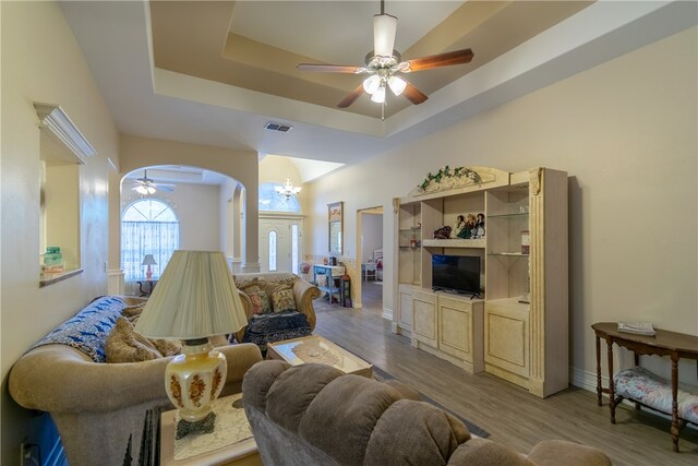 living room with wood-type flooring, ceiling fan with notable chandelier, and a raised ceiling