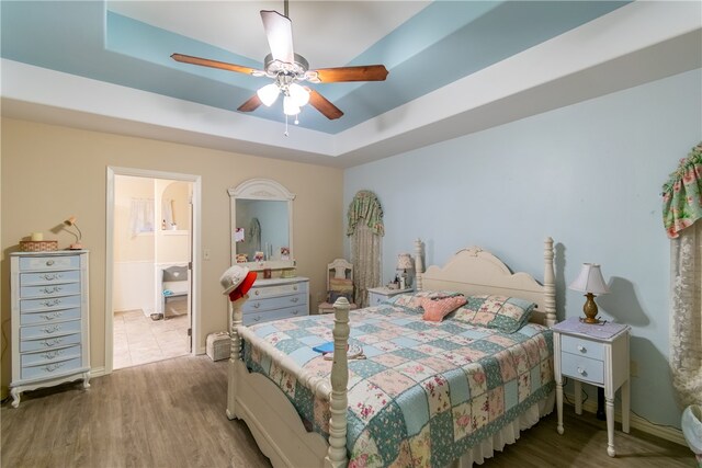 bedroom with a tray ceiling, hardwood / wood-style floors, ceiling fan, and ensuite bath