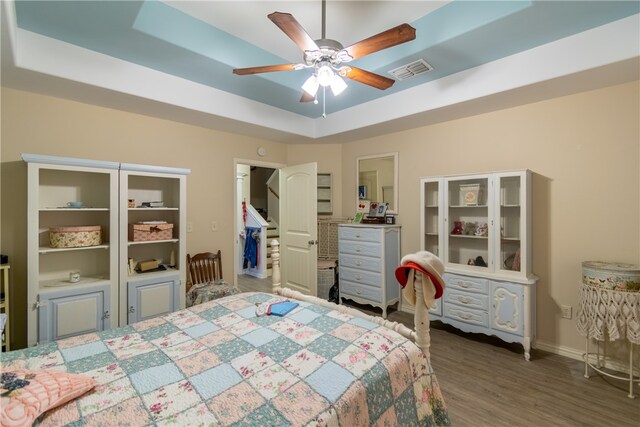 bedroom with hardwood / wood-style floors, ceiling fan, and a raised ceiling