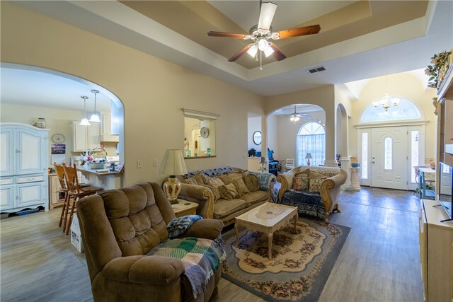 living room featuring ceiling fan with notable chandelier, a raised ceiling, and light hardwood / wood-style flooring