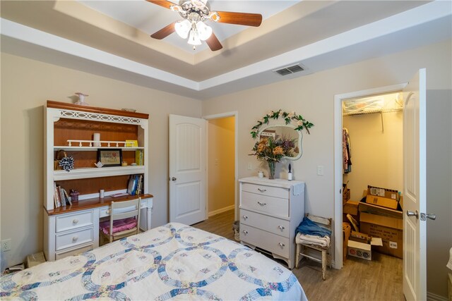 bedroom featuring ceiling fan, a raised ceiling, light hardwood / wood-style flooring, a walk in closet, and a closet