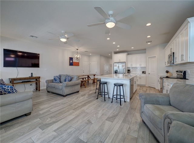 living room featuring ceiling fan with notable chandelier, light wood-type flooring, and sink