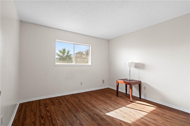 spare room with a textured ceiling, baseboards, and wood finished floors