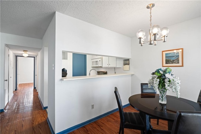 dining area featuring dark wood-style floors, a textured ceiling, a notable chandelier, and baseboards