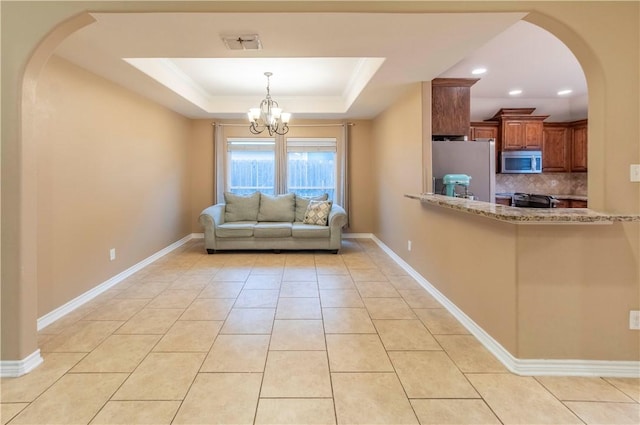 unfurnished living room featuring ornamental molding, light tile patterned floors, an inviting chandelier, and a tray ceiling