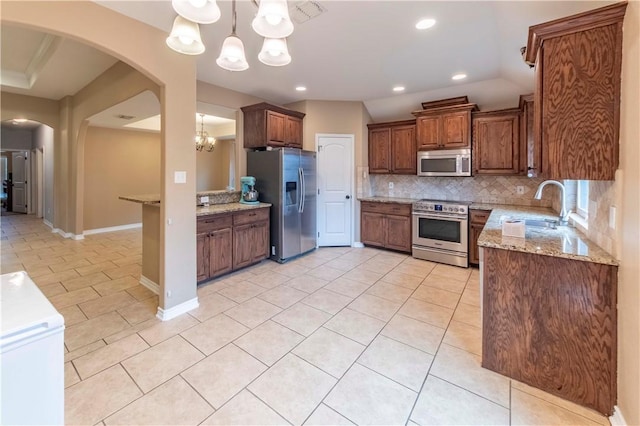 kitchen with sink, decorative light fixtures, appliances with stainless steel finishes, light stone countertops, and backsplash