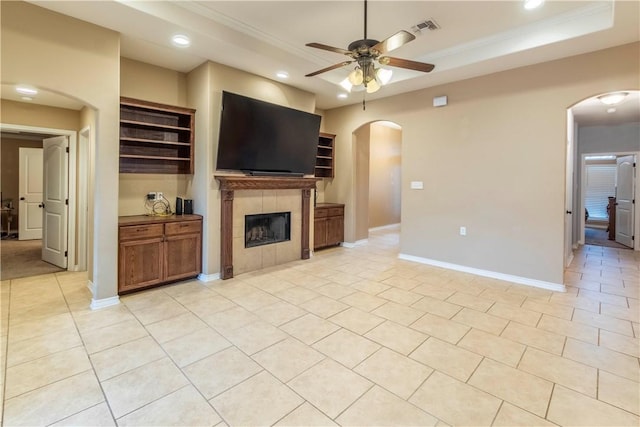 living room with ceiling fan, a fireplace, a raised ceiling, and light tile patterned floors