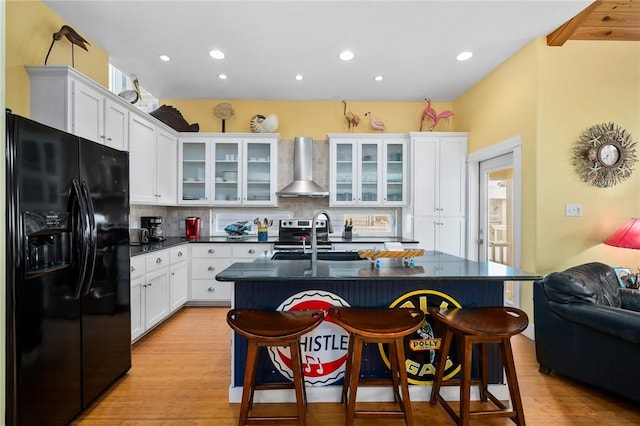 kitchen featuring black fridge, wall chimney range hood, sink, and a kitchen island with sink