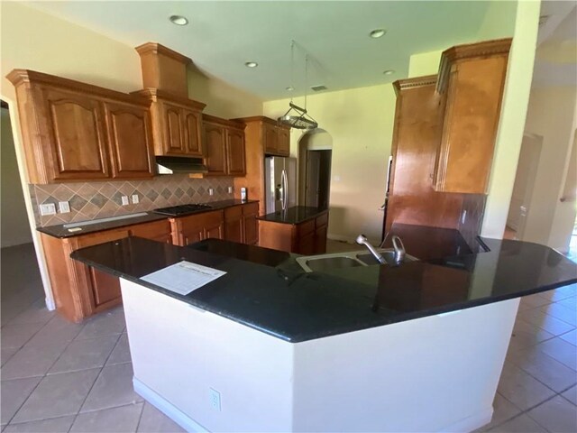 kitchen featuring stainless steel refrigerator with ice dispenser, a center island, dark countertops, tasteful backsplash, and light tile patterned flooring