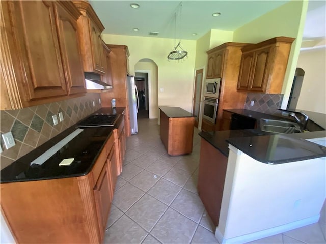 kitchen with appliances with stainless steel finishes, arched walkways, a kitchen island, under cabinet range hood, and dark countertops
