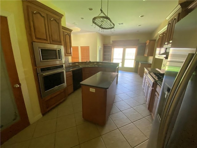 kitchen featuring appliances with stainless steel finishes, a peninsula, dark countertops, light tile patterned floors, and hanging light fixtures