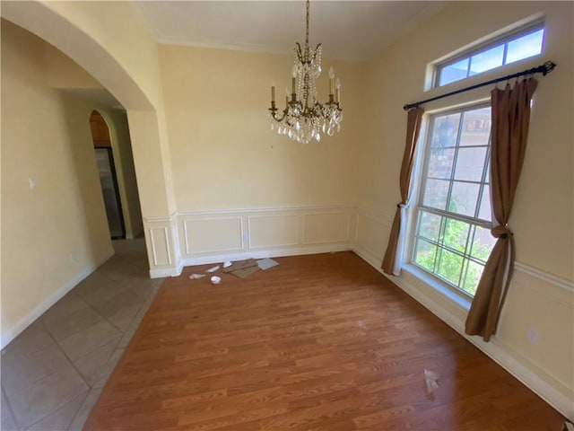 unfurnished dining area featuring plenty of natural light, arched walkways, a chandelier, a decorative wall, and crown molding