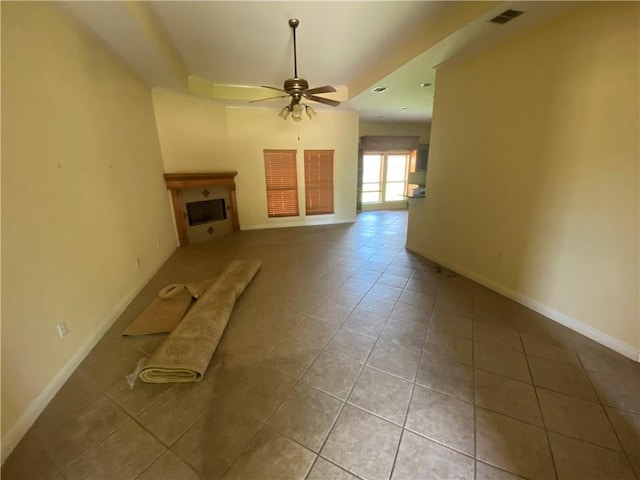unfurnished living room featuring tile patterned flooring, ceiling fan, a tray ceiling, and a fireplace