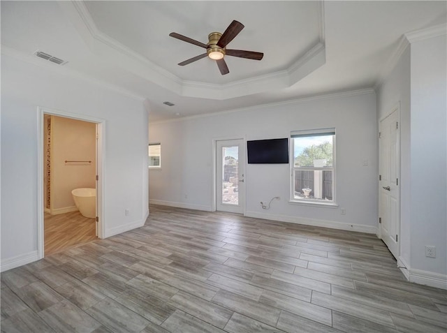 unfurnished bedroom with a tray ceiling, crown molding, wood finished floors, connected bathroom, and ceiling fan