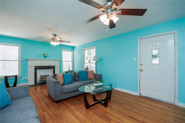 living room with a fireplace, ceiling fan, and dark wood-type flooring