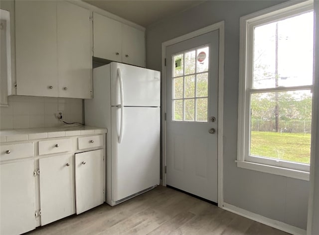 kitchen with white fridge, white cabinetry, decorative backsplash, tile countertops, and light hardwood / wood-style flooring