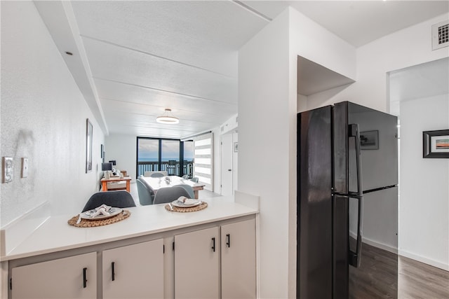 kitchen with black refrigerator, dark wood-type flooring, and white cabinets