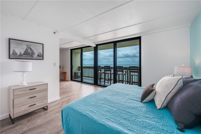 bedroom with a textured ceiling, a wall of windows, light hardwood / wood-style floors, and access to exterior