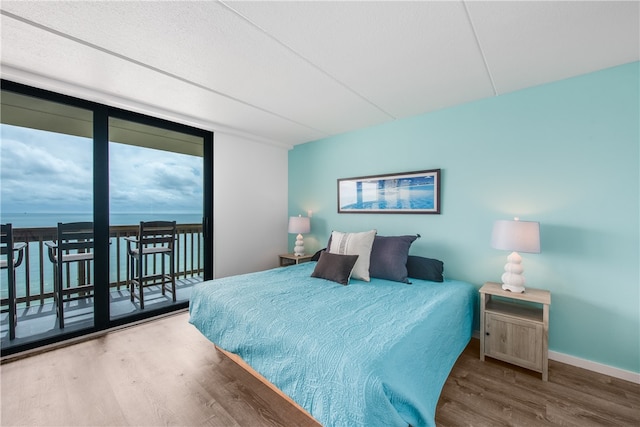 bedroom with access to exterior, a water view, and wood-type flooring