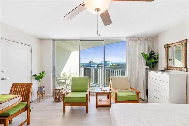 bedroom with access to exterior, a city view, expansive windows, ceiling fan, and light wood-type flooring