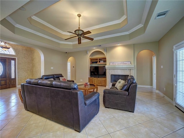 tiled living room featuring built in shelves, a raised ceiling, ceiling fan, and a tiled fireplace