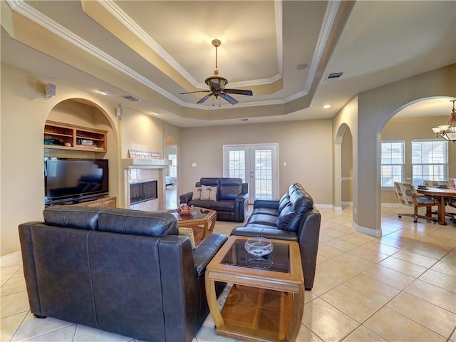 tiled living room featuring french doors, ceiling fan with notable chandelier, a raised ceiling, crown molding, and built in features