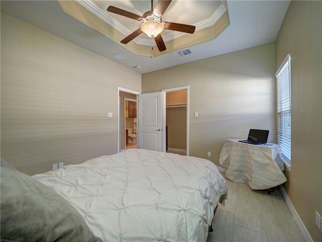 bedroom with a raised ceiling, a walk in closet, crown molding, ceiling fan, and a closet