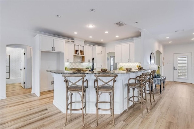 kitchen with white cabinetry, arched walkways, and dark stone countertops