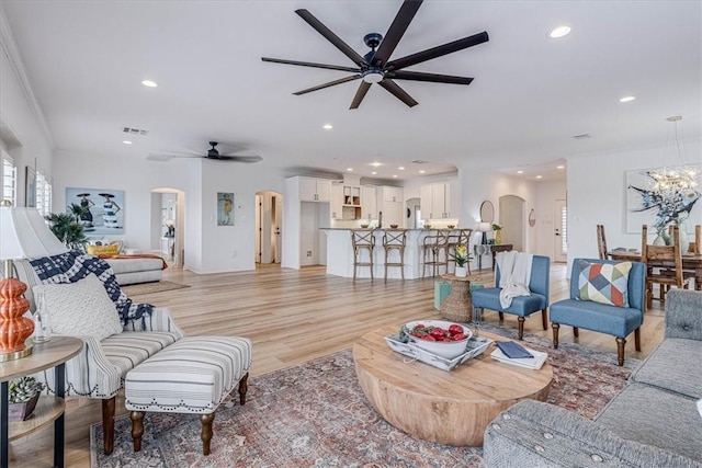 living area featuring arched walkways, recessed lighting, ceiling fan with notable chandelier, visible vents, and light wood finished floors