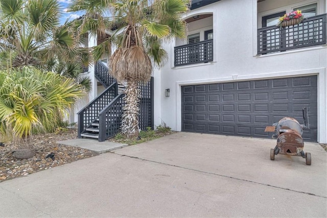 view of side of property with driveway, an attached garage, stairs, and stucco siding