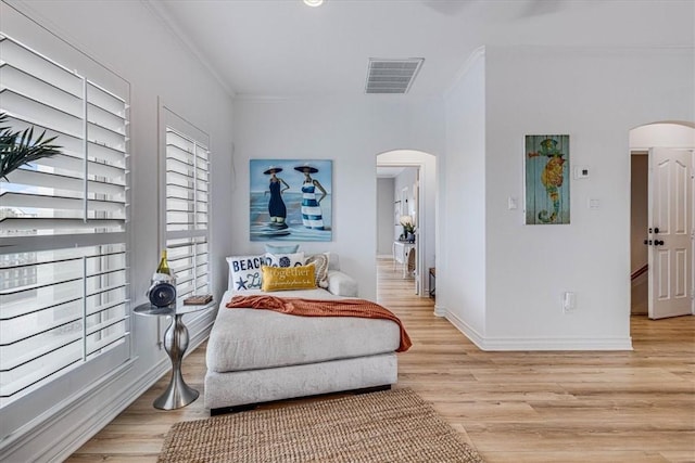 sitting room featuring arched walkways, visible vents, baseboards, light wood-style floors, and ornamental molding