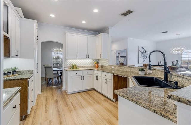 kitchen featuring arched walkways, light wood finished floors, visible vents, a sink, and light stone countertops