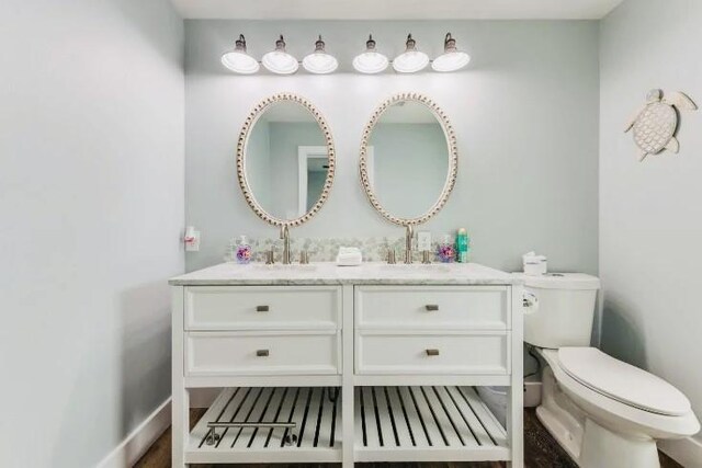 bathroom featuring toilet, double vanity, baseboards, and a sink