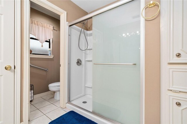 bathroom featuring a shower with shower door, tile patterned floors, and toilet