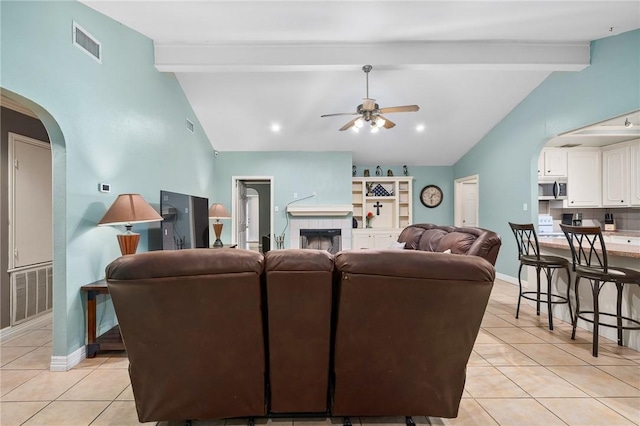 tiled living room featuring ceiling fan, a tiled fireplace, and lofted ceiling with beams