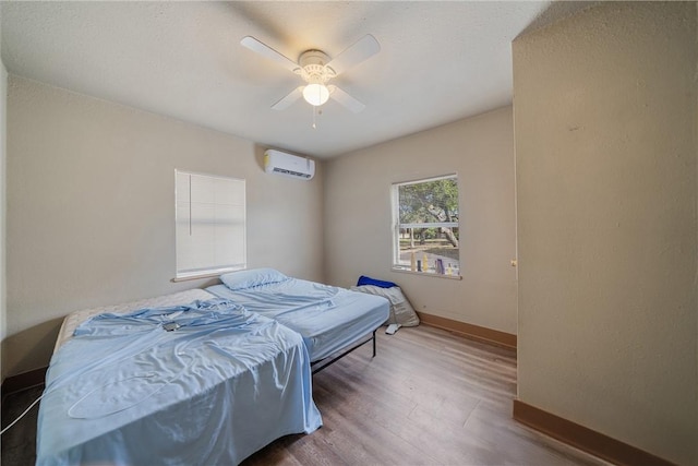 bedroom with a wall mounted air conditioner, ceiling fan, and hardwood / wood-style flooring