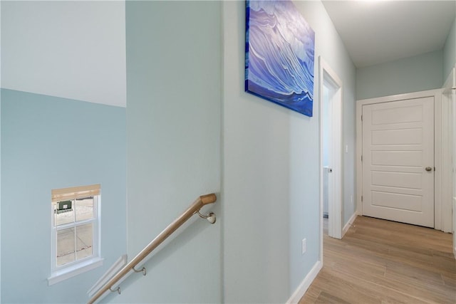 hall featuring baseboards, an upstairs landing, and light wood-style flooring