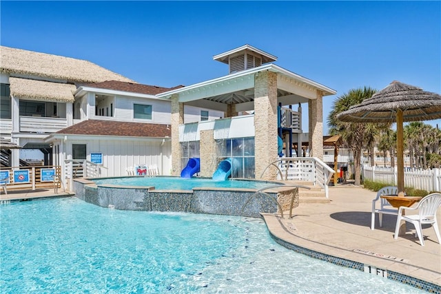 community pool featuring a jacuzzi, a patio, a water slide, and fence