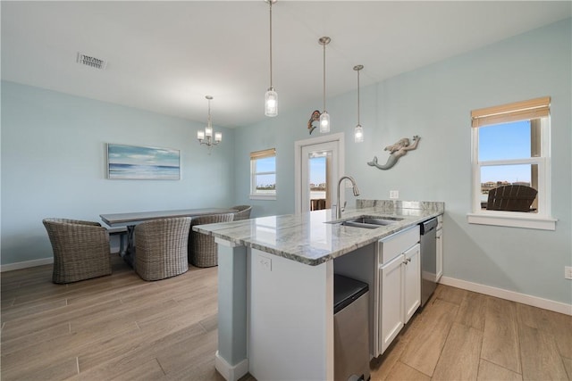 kitchen with light wood-type flooring, light stone counters, a peninsula, stainless steel dishwasher, and a sink